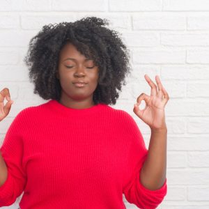 Young african american plus size woman over white brick wall relax and smiling with eyes closed doing meditation gesture with fingers. Yoga concept.